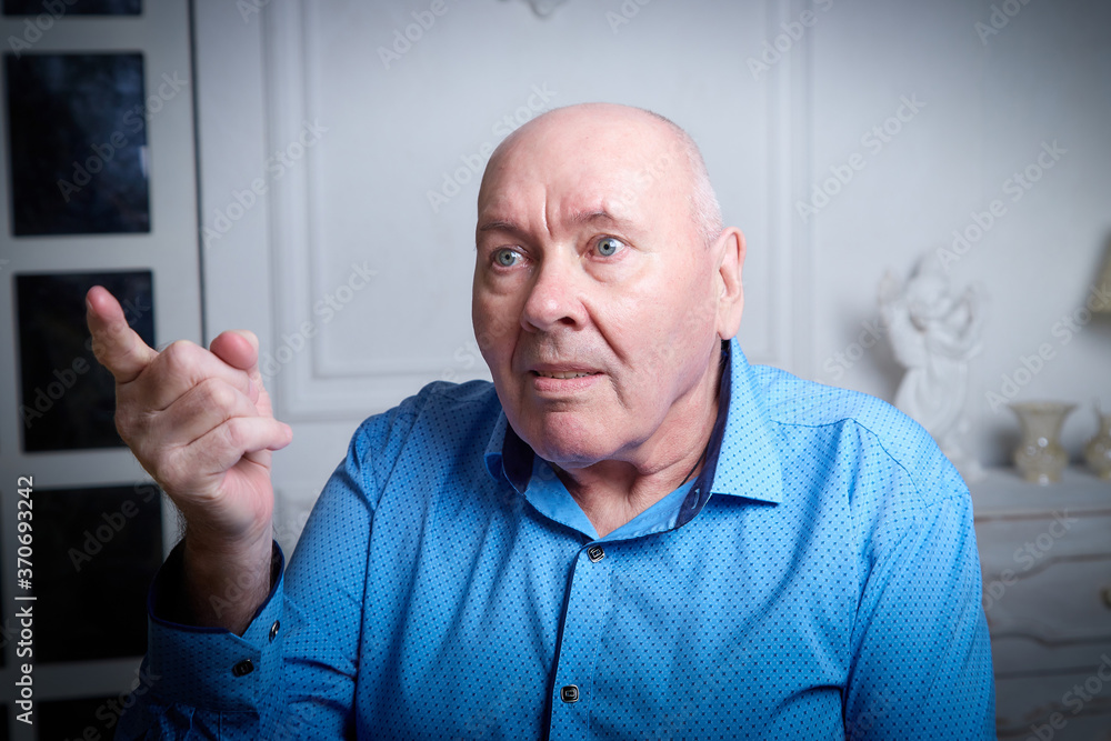 Portrait of an elderly bald man in a blue shirt in the room. A poor pensioner lives alone. Portrait of an elderly bald man in a blue shirt in the room. A poor pensioner lives alone.
