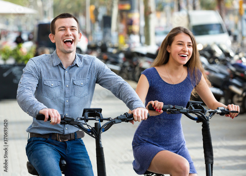 Charming smiling man and woman with electrkc bikes in vacation on city street