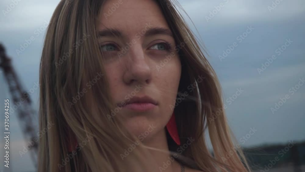 Handheld shooting. Close-up, faces of a beautiful, cute, sad, pensive girl with long blond hair, blue eyes. The camera moves around the blonde. The wind develops hair on a background of cloudy sky Handheld shooting. Close-up, faces of a beautiful, cute, sad, pensive girl with long blond hair, blue eyes. The camera moves around the blonde. The wind develops hair on a background of cloudy sky