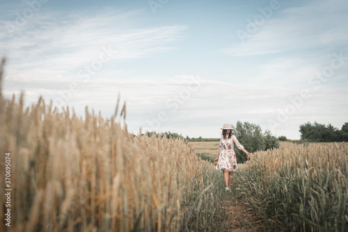Beautiful young brunette girl in a wheat field walking on the trail
