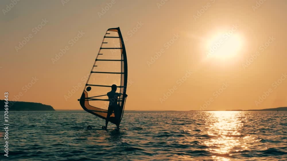 A man is windsurfing in the sea at sunset A man is windsurfing in the sea at sunset