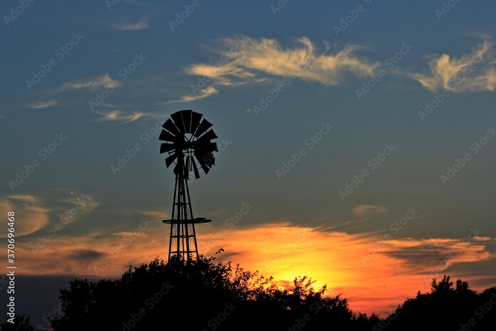 windmill at sunset with colorful clouds and tree's out in the country in Kansas. windmill at sunset with colorful clouds and tree's out in the country in Kansas.