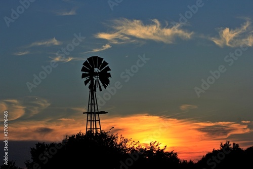 windmill at sunset with colorful clouds and tree's out in the country in Kansas.