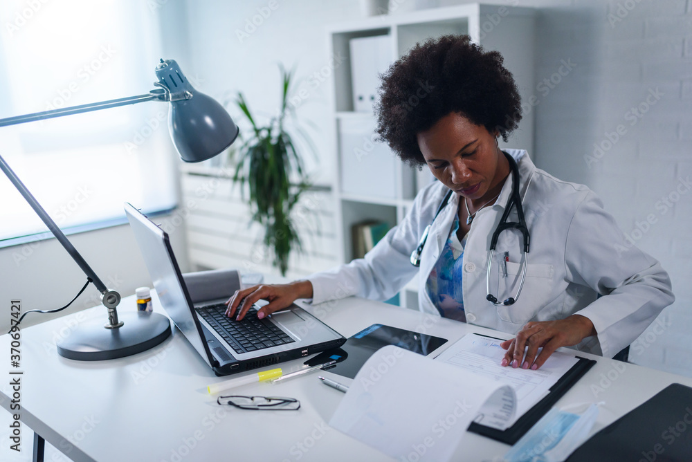 Woman doctor with stethoscope looking at medical papers at her office working hard