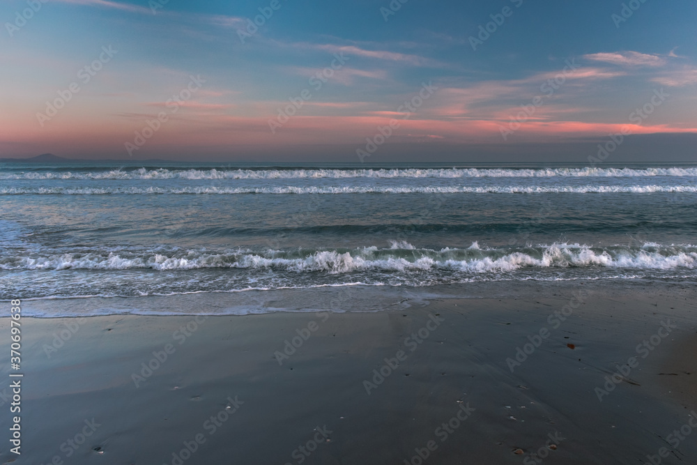 Sea with waves, sea foam and sandy beach at dusk