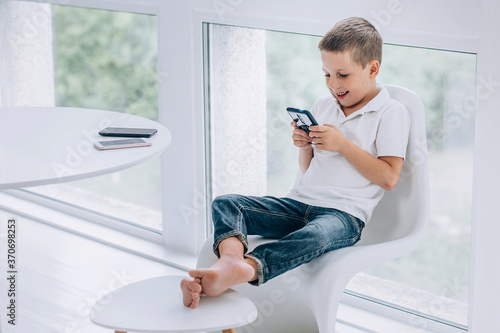 teen boy sits on a chair cross-legged and plays on the phone