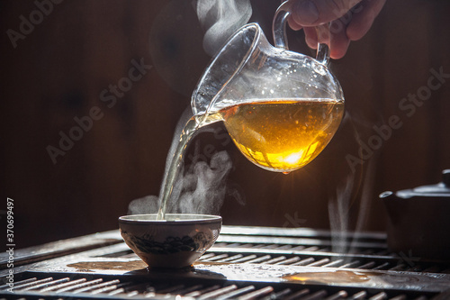 hand pours green chinese tea from a glass teapot