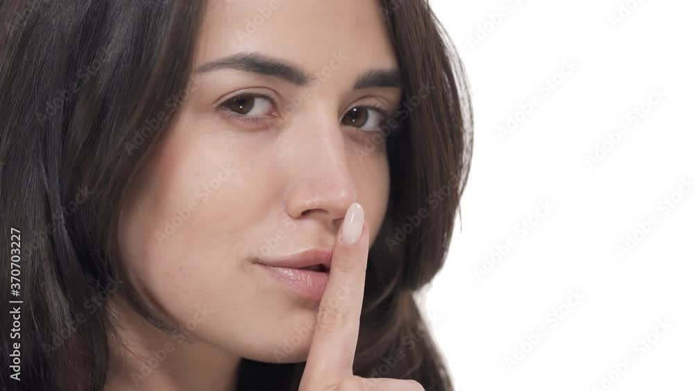 Close up of attractive Caucasian woman turning face to camera, showing silence gesture and winking. Macro shot with copy space. Isolated on white background Close up of attractive Caucasian woman turning face to camera, showing silence gesture and winking. Macro shot with copy space. Isolated on white background