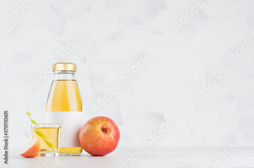 Organic yellow transperent pear juice in glass bottle mock up with blank label, straw, wine glass, fruit slice on white wood table in light interior, template for packaging, advertising.