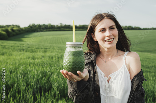 Young Stylish Girl in White Dress and Denim Jacket Holds Green Smoothie Fresh Drink in the Wheat Field