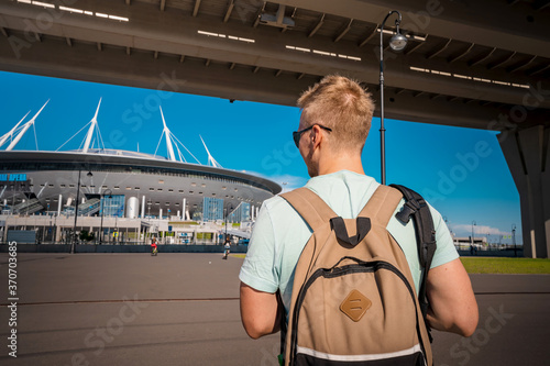 A young man blond with a backpack walking on Krestovsky island under the bridge Western high speed diameter road with a view of the stadium in Saint Petersburg photo