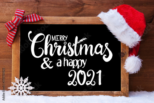 Chalkboard With English Calligraphy Merry Christmas And A Happy 2021. Christmas Decoration Like Santa Hat And Bow. Wooden Background With Snow