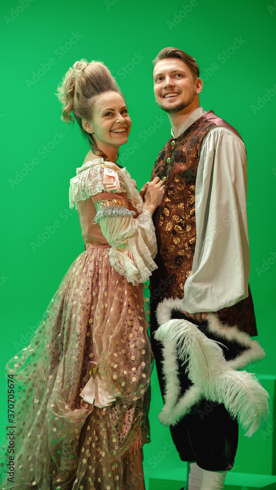 Fototapeta premium On Big Film Studio Two Talented Actors of Female and Male Playing a Beautiful Lovely Couple Wearing Renaissance Clothes and Smiling on Camera. The Scene on Green Screen.