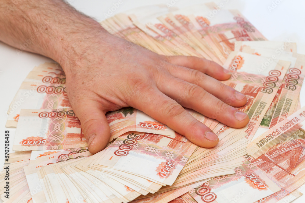 A man's hand counts and shifts a large number of five thousand rubles bills into a stack