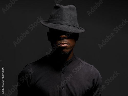 portrait of a young African man in a black hat. Black background studio photography