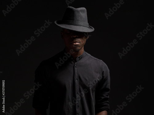 portrait of a young African man in a black hat. Black background studio photography