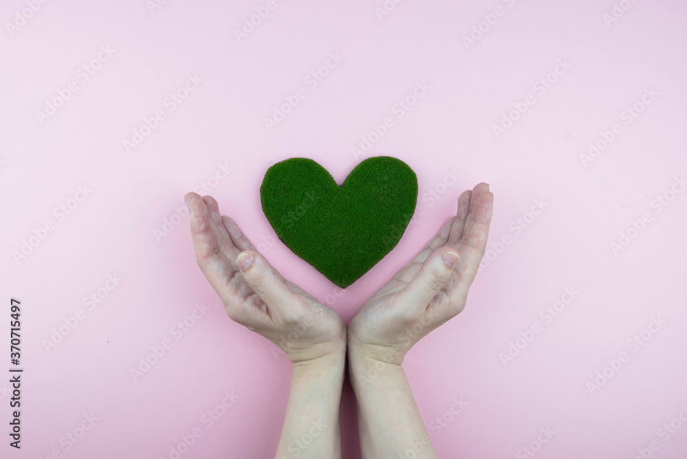 Earth day, ecology and Environmental preservation concept. Hands holding green heart from grass on pink background. Love nature and save the planet and world.