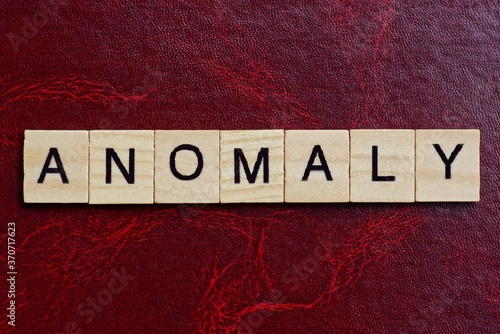 text the word anomaly from gray wooden small letters with black font on an red table photo