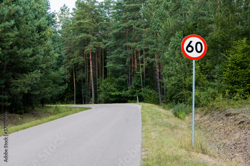 Speed limit sign with trees behind. Maximum sixty kilometers per hour. Safety on road in forest background. White round sign red border line.
