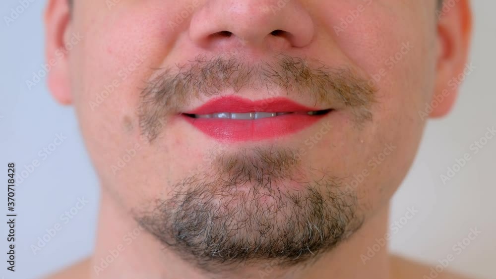 Man with red lipstick on lips giving a kiss on white background, mouth closeup. LGBT, gey, free love concept. Bearded unrecognizable young guy with moustache. Man with red lipstick on lips giving a kiss on white background, mouth closeup. LGBT, gey, free love concept. Bearded unrecognizable young guy with moustache.