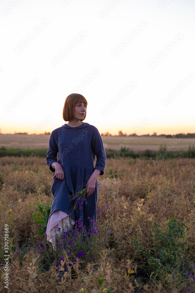 Young redhead woman with  
freckles in vintage handmade dress walk in fields with flowers 