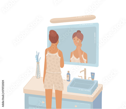 Young woman looking at bathroom mirror moisturizing to protects her skin