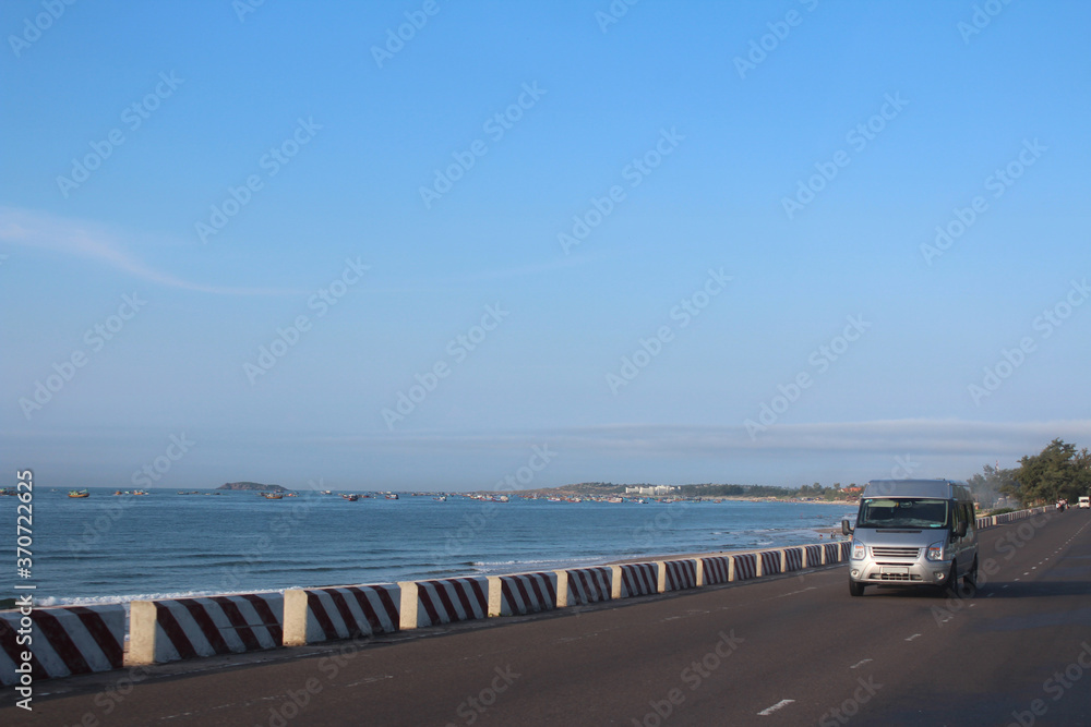 Sea with the fishing boats and car on the road in the sunny morning at Mui Ne