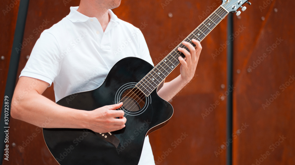 Close up photo of young man playing at guitar outdoor.