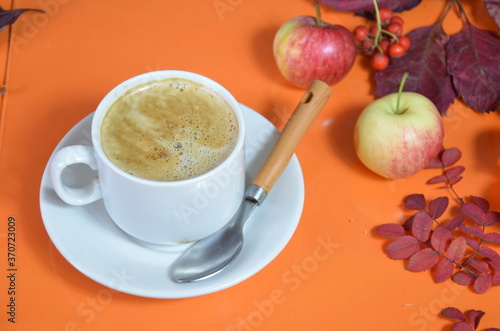 Autumn leaves and hot steaming cup of coffee. Wooden table against golden sunset or sunrise light background. Fall season, leisure time and coffee break concept