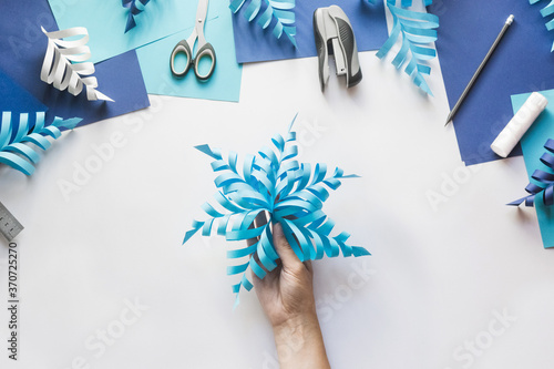 How to make paper beautiful Christmas toy snowflake to decorate room with children at home. Step by step instructions. Top view. Hands making DIY winter craft project. Step 11. Enjoy ready toy
