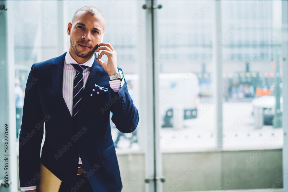 Serious banker having mobile conversation about work with colleague standing near publicity area,self-confident executive manager in formalwear discussing business plans during phone conversation. Serious banker having mobile conversation about work with colleague standing near publicity area,self-confident executive manager in formalwear discussing business plans during phone conversation.