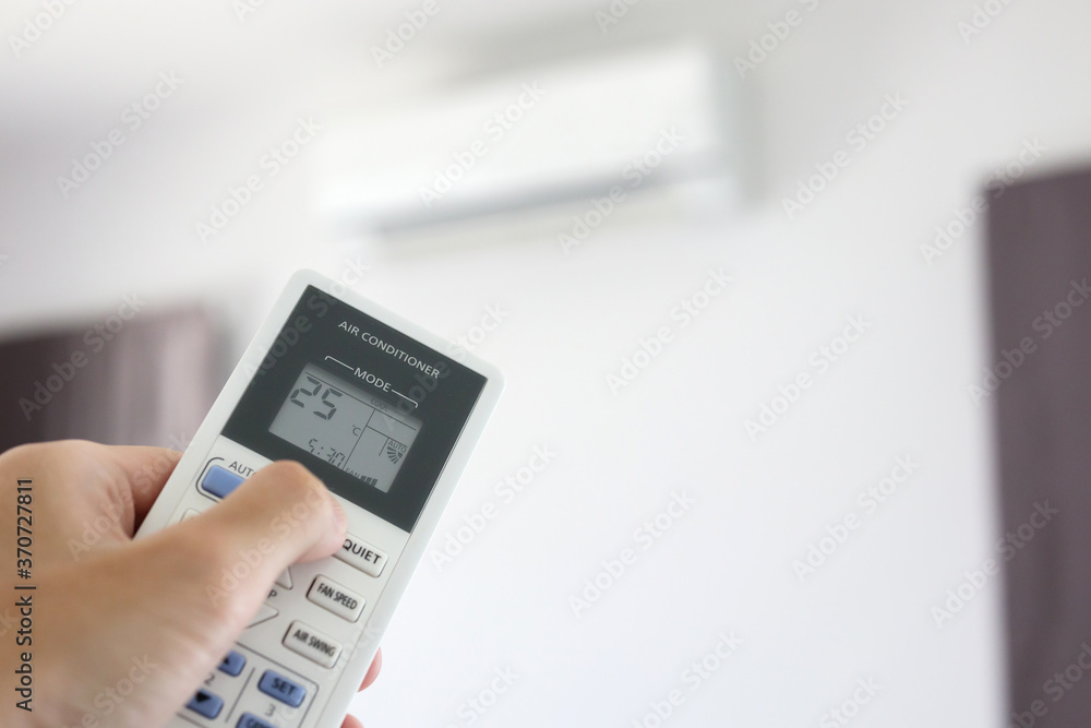 Hand with remote control directed on air conditioner inside the room Hand with remote control directed on air conditioner inside the room
