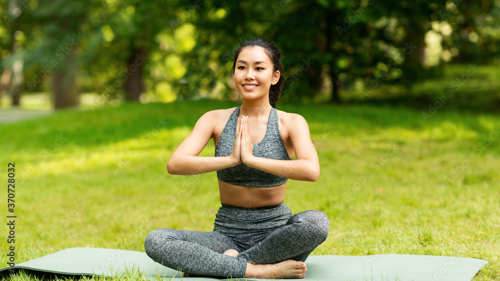 Calm Asian girl meditating in lotus pose during her yoga class outdoors Calm Asian girl meditating in lotus pose during her yoga class outdoors