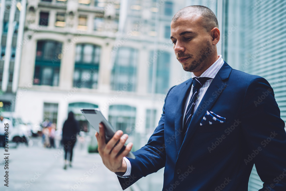 Pensive male entrepreneur in elegant wear making banking and paying for service online using tablet outdoors,prosperous trader checking news via application on portable pc standing near publicity area Pensive male entrepreneur in elegant wear making banking and paying for service online using tablet outdoors,prosperous trader checking news via application on portable pc standing near publicity area