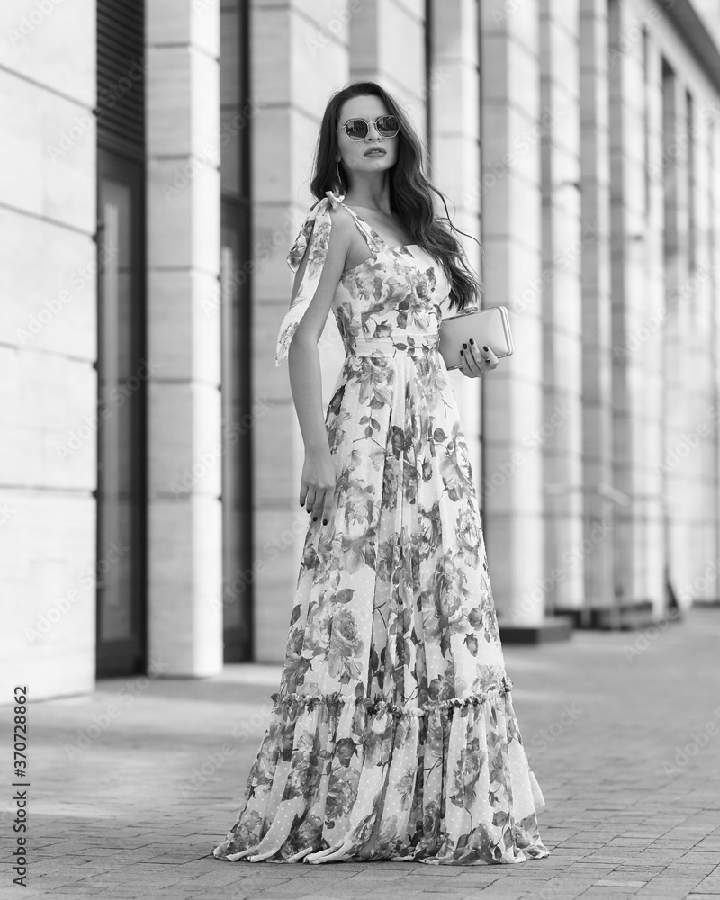 Elegant woman in long pink summer dress with floral print walking at city street. Outdoor full length portrait. Pretty female model Elegant woman in long pink summer dress with floral print walking at city street. Outdoor full length portrait. Pretty female model