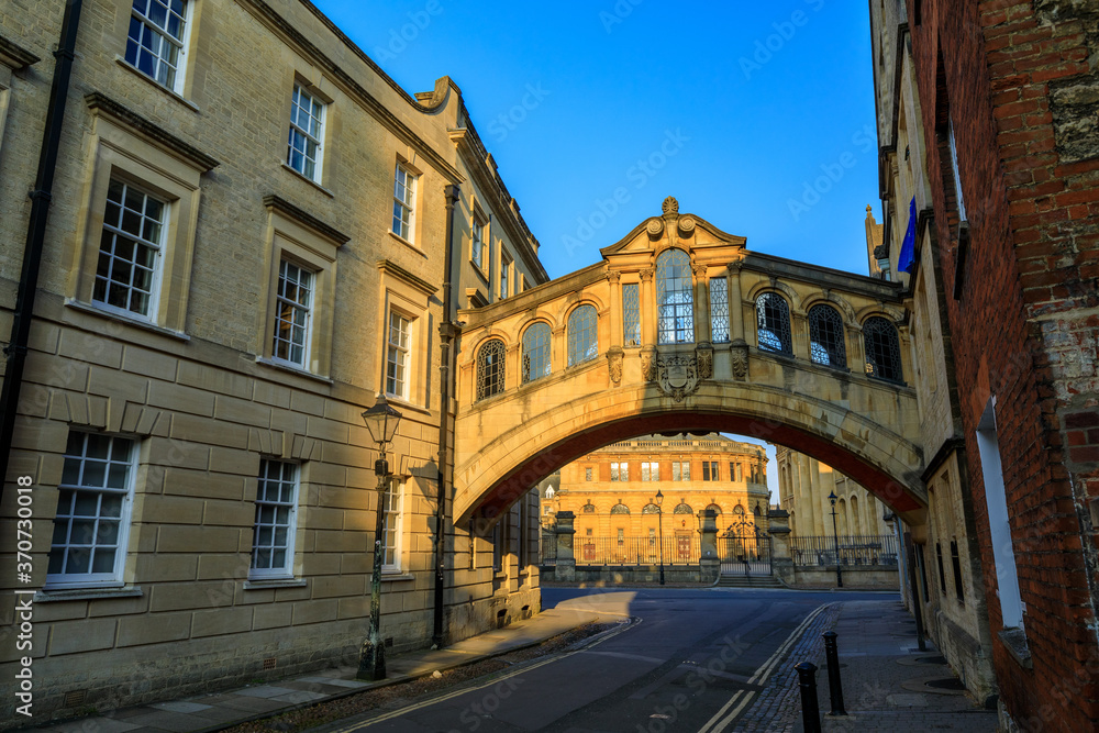 Hertford Bridge, Bridge of Sighs, in Oxford at sunrise with Sheldonian Theatre behind it and no people around, early in the morning on a clear day with blue sky. Oxford, England, UK.