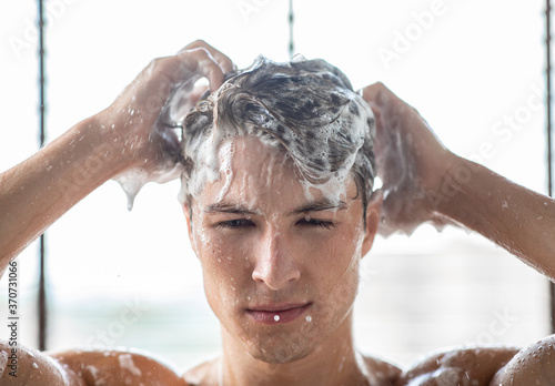 Handsome young man washing hair with shampoo