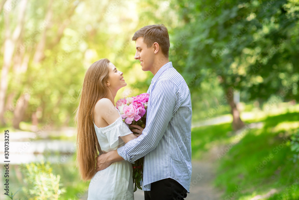 Lovely girl with bouquet of peonies hugging her boyfriend on romantic date at park Lovely girl with bouquet of peonies hugging her boyfriend on romantic date at park