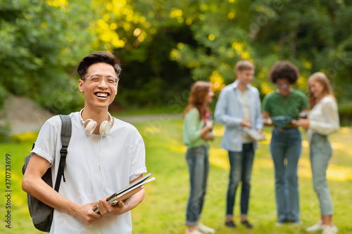 Portrait Of Happy Asian Student Guy With Workbooks And Backpack Posing Outdoors