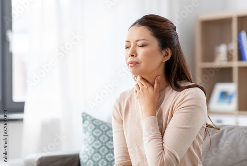 Free Download health, cold and people concept - sad sick young asian woman with sore throat at home - GFXLoad