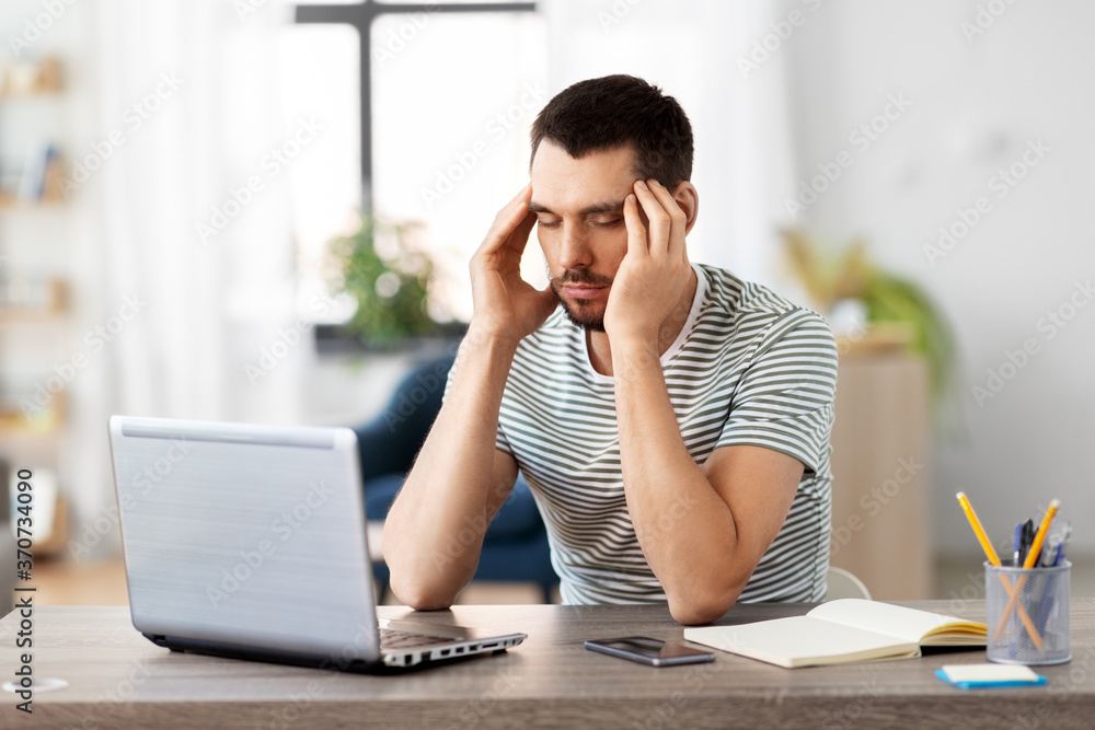 remote job, technology and people concept - stressed young man with laptop computer having headache at home office remote job, technology and people concept - stressed young man with laptop computer having headache at home office