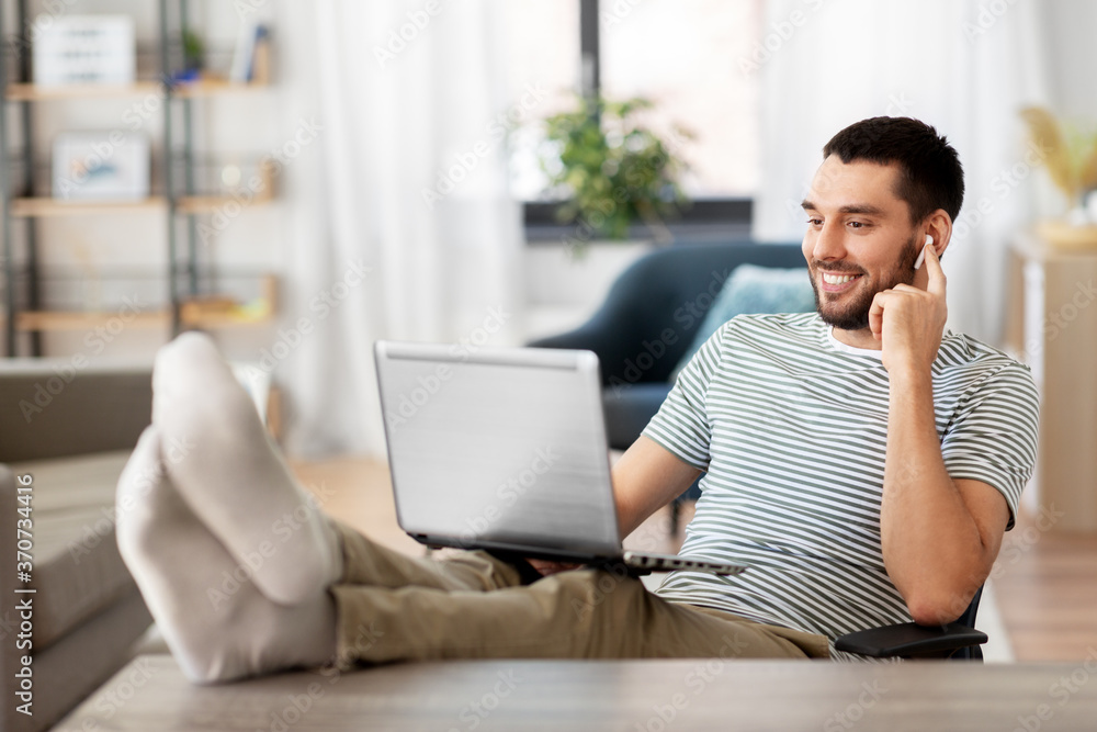 technology, remote job and lifestyle concept - happy smiling man with laptop computer and earphones resting feet on table at home office technology, remote job and lifestyle concept - happy smiling man with laptop computer and earphones resting feet on table at home office