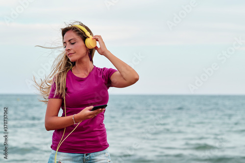 young woman at the beach hearing music with yellow headphones