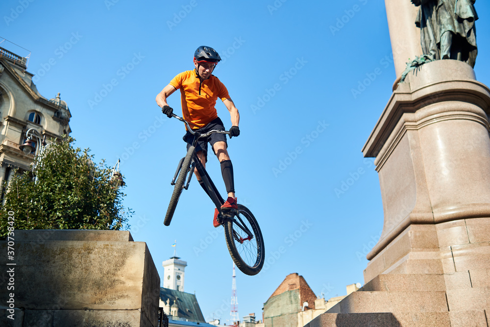 Obraz premium View from below extreme man holding a sport bike and hanging in air. Cyclist looking down when doing trick. Concept of trick.