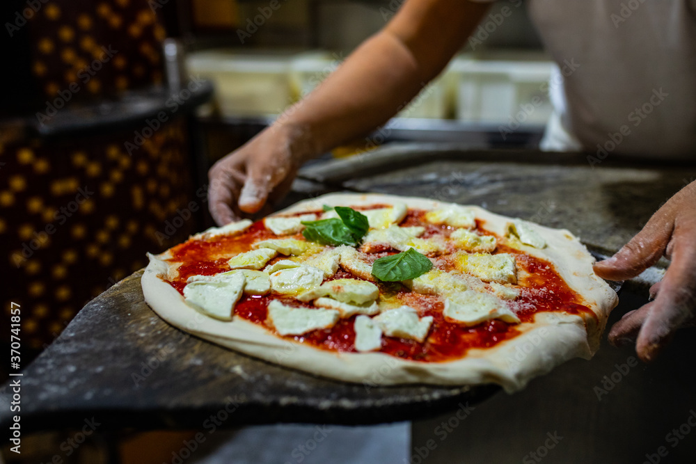 Pizzaiolo mentre stende sulla pala di legno da forno una pizza margherita napoletana pronta da infornare