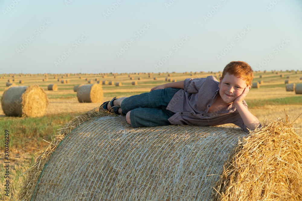 The red-haired boy lies on top of a straw bale on a wheat field The red-haired boy lies on top of a straw bale on a wheat field