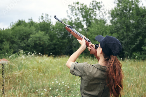 Military woman holding a gun aiming hunting green leaves 