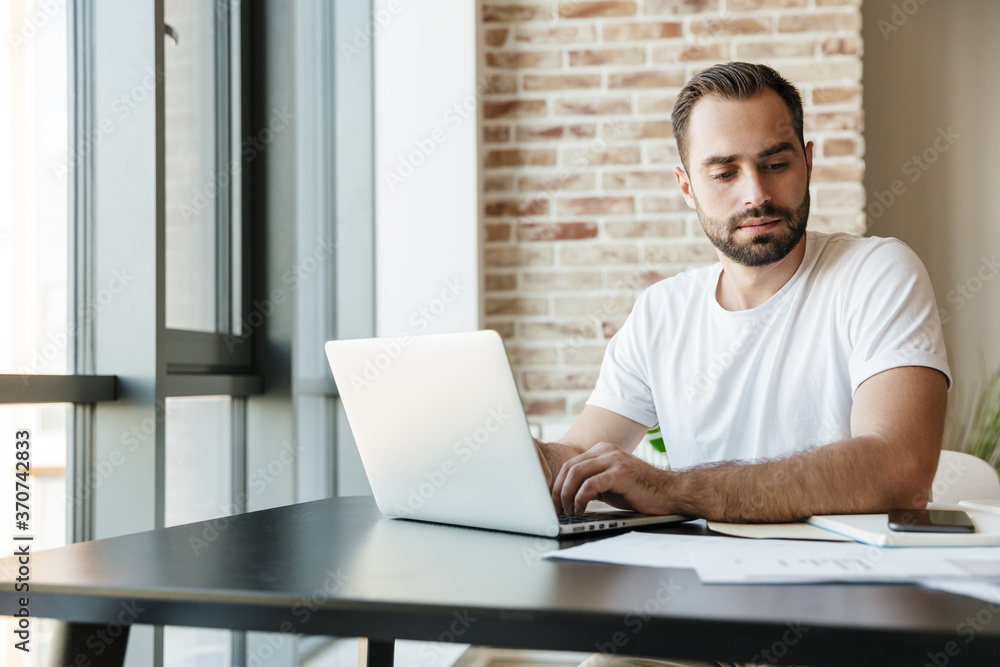 Image of young man working with laptop while sitting at table Image of young man working with laptop while sitting at table