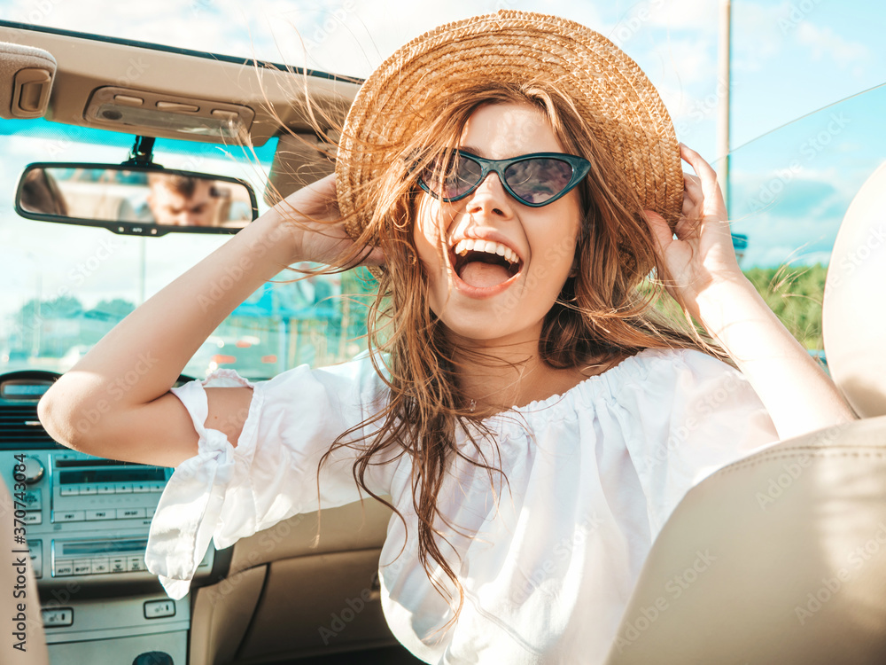 Portrait of young beautiful and smiling hipster girl in convertible car. Sexy carefree woman driving cabriolet. Positive model riding and having fun in sunglasses and hat - obrazy, fototapety, plakaty 