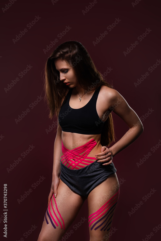 Obraz premium Kinesiology taping. Young female athlete on red background with kinesiology tape on tummy and hips. Fat lose, cellulite removal, sport physical therapy,recovery concept.